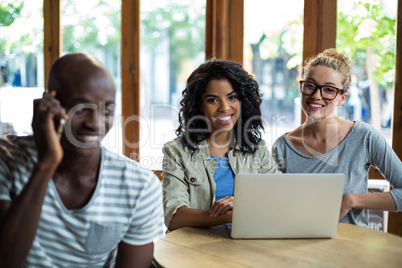 Man talking on mobile phone while friends using laptop in background