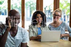 Man talking on mobile phone while friends using laptop in background