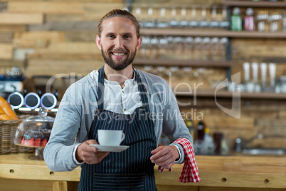 Portrait of smiling waiter offering cup of coffee
