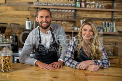 Portrait of smiling waiter and waitress leaning at counter