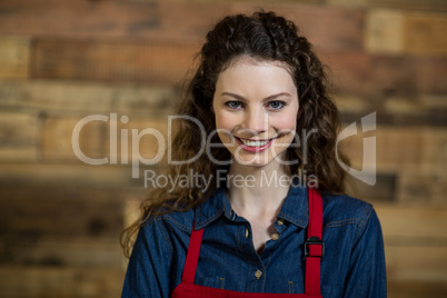 Portrait of smiling waitress standing against wooden wall