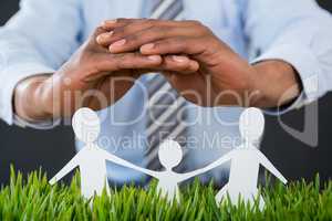 Businessman protecting paper cut out family, house and car with hand