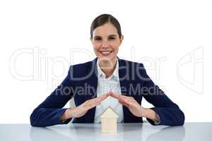 Smiling businesswoman protecting house model with hands