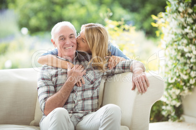 Senior woman kissing man on cheek in living room