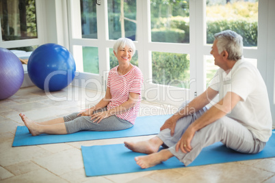 Happy senior couple interacting while performing exercise on exercise mat