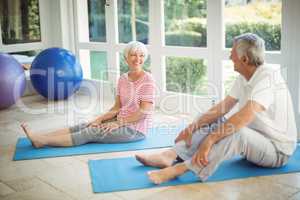 Happy senior couple interacting while performing exercise on exercise mat