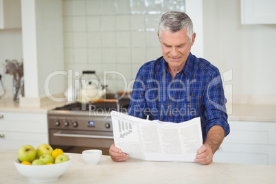 Senor man reading newspaper in kitchen