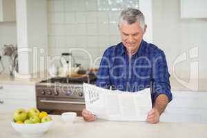 Senor man reading newspaper in kitchen