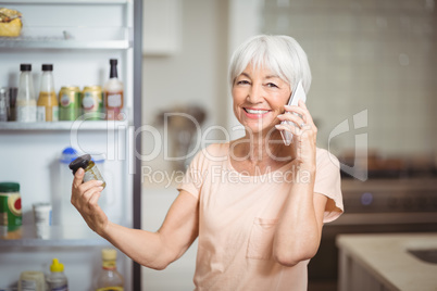 Senior woman looking at jar while talking on mobile phone in kitchen
