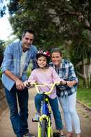 Portrait of happy parents assisting daughter to ride bicycle in park