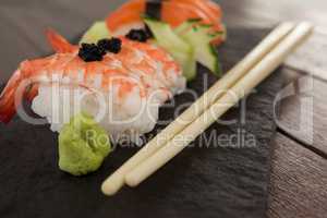 Nigiri sushi served with chopsticks in black stone slate on wooden table