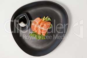 Four sashimi sushi served with soy sauce in black plate