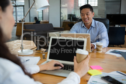 Business executives interacting with each other while using laptop at desk