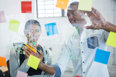 Business colleagues discussing over sticky notes on glass