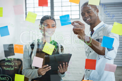 Business colleagues discussing over sticky notes on glass