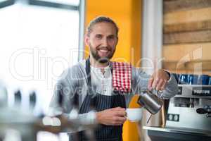 Smiling waiter making cup of coffee at counter in cafe