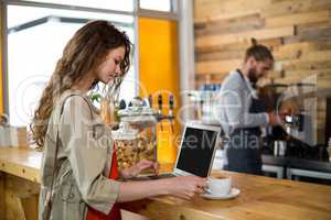 Woman standing at counter and using laptop while having coffee