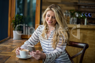 Smiling woman using mobile phone while having coffee