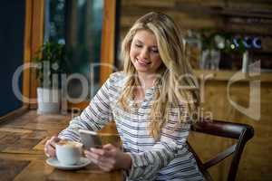 Smiling woman using mobile phone while having coffee