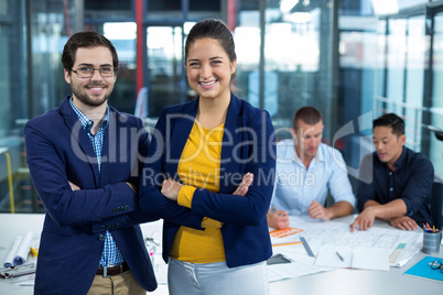 Male and female business executive smiling while colleague interacting over blueprint in background