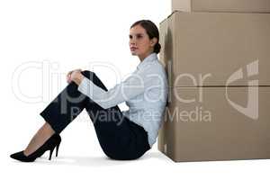 Businesswoman leaning on cardboard boxes against white background