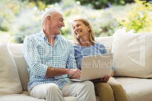Senior couple interacting with each other while using laptop in living room
