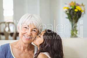 Granddaughter kissing grandmother on cheek in living room