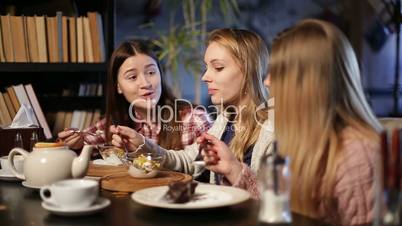 Three young teenage girls eating desserts in cafe