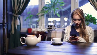 Cute girl typing message on smart phone in cafe