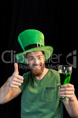 portrait of cheerful man holding glass of beer on St.Patrick's day and showing thumb up on black