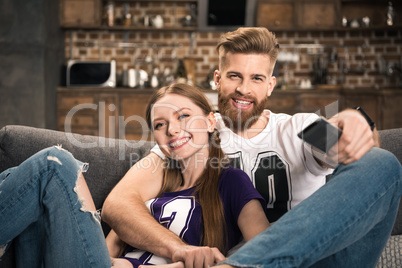 portrait of smiling couple sitting on sofa and watching movie at home