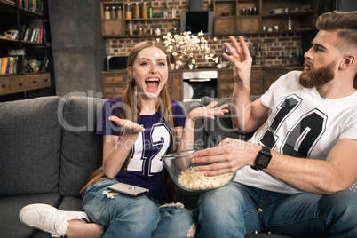 Portrait of excited couple throwing popcorn while watching movie at home