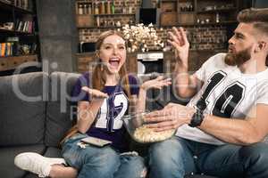 Portrait of excited couple throwing popcorn while watching movie at home