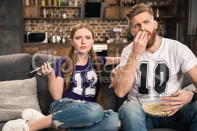 portrait of concentrated couple watching movie with popcorn at home