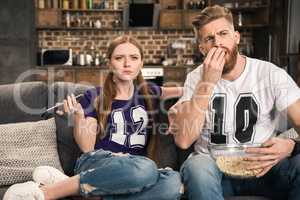 portrait of concentrated couple watching movie with popcorn at home