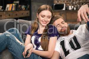 portrait of smiling woman looking at sleeping man while watching movie at home