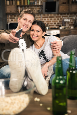 portrait of happy couple watching movie with beer and popcorn at home