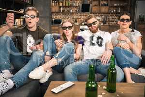 shocked young friends in 3D glasses watching movie at home