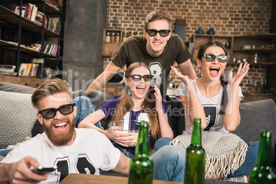 excited young friends in 3D glasses watching movie on sofa at home