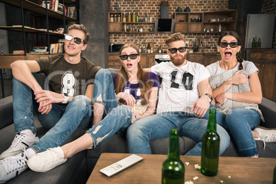 young friends in 3D glasses watching movie with beer at home