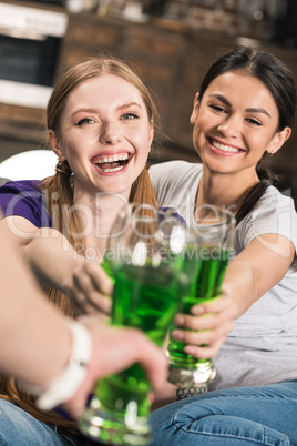 Happy young women clinking glasses with green beer while celebrating St Patricks Day