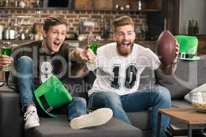 Excited young men with beer glasses watching football match at st patricks day