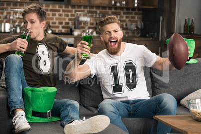 Excited young men with beer glasses watching football match at st patricks day