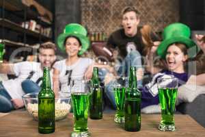 Green beer in bottles and glasses near friends celebrating st patricks day