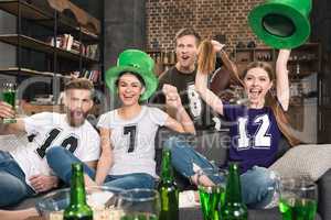 Excited young friends in hats cheering and drinking beer at st patricks day