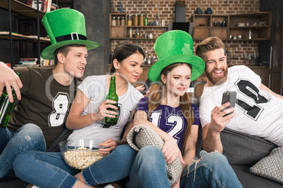 Smiling young friends drinking beer and using smartphone, st patricks day concept