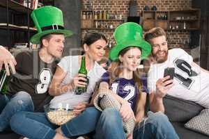 Smiling young friends drinking beer and using smartphone, st patricks day concept