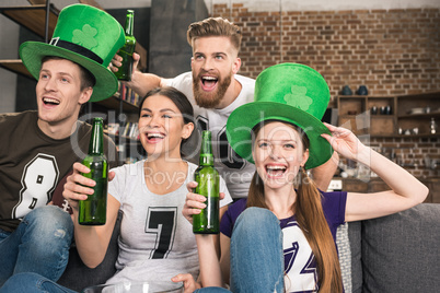 Happy young friends in green hats drinking beer and celebrating st patricks day