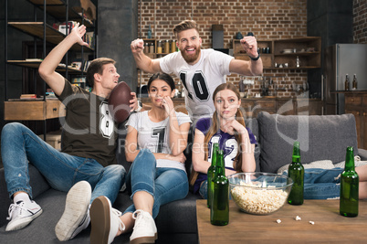 Bored young women sitting near excited men supporting favorite football team at home