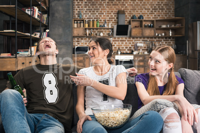 Happy young friends sitting on sofa and eating popcorn from glass bowl